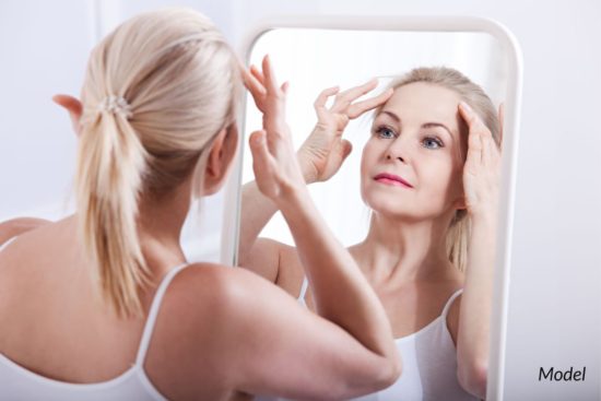 Woman looking at her face in mirror after a facial procedure, such as facelift surgery.