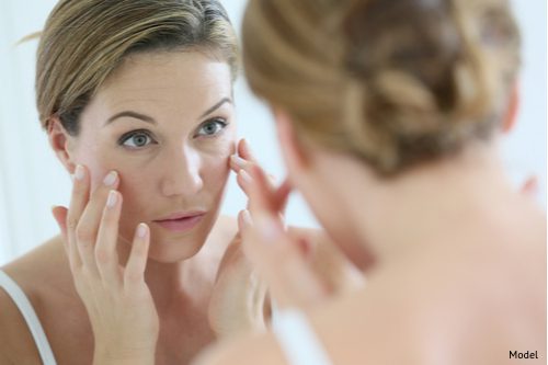 Woman in her 30s looking in mirror, wondering if she could benefit from a facelift.