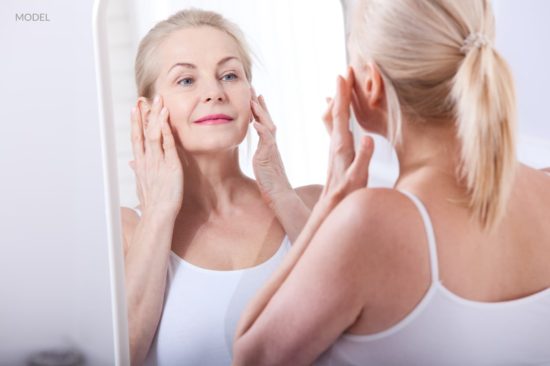 Middle aged woman looking at wrinkles in mirror. Before-after anti-aging facelift treatment.