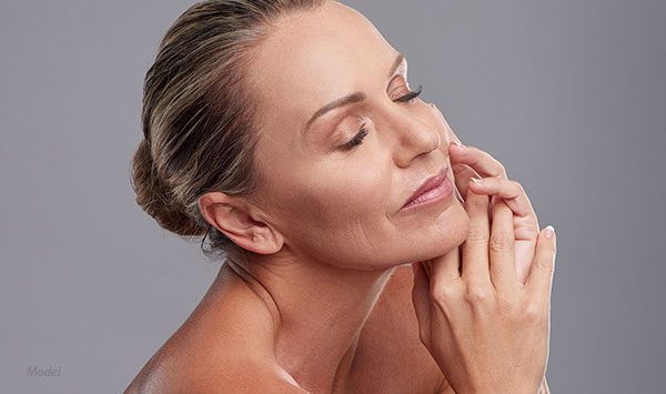 Profile headshot of middle aged woman with her eyes closed and hands rubbing her skin