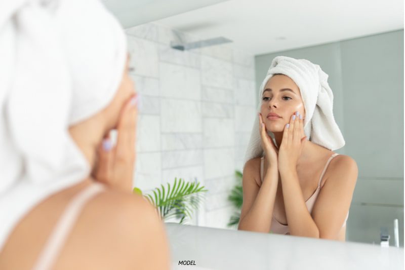 Young woman applying skim cream while looking in mirror.