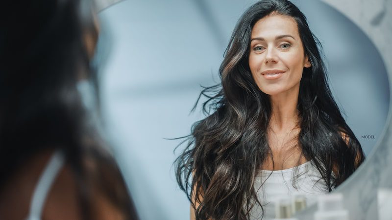 A beautiful middle-aged woman looks in the mirror.