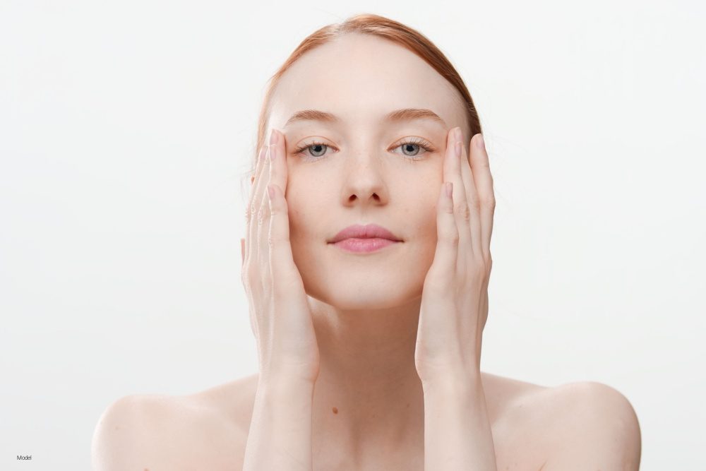 Beautiful redhead young woman touches her face with both hands stretching it a bit