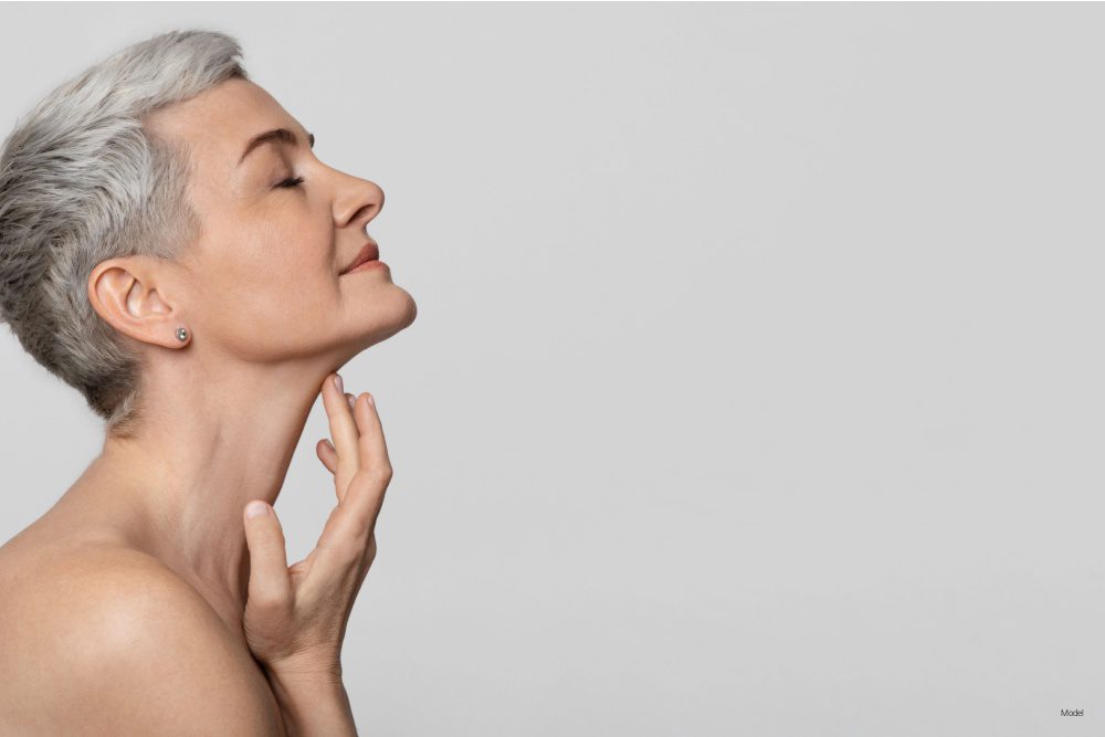Profile of beautiful middle-aged woman touching soft skin on her neck over light background.